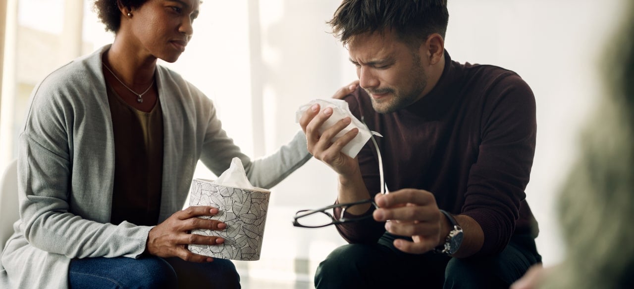 A support worker offering tissues and a steady hand to someone in distress